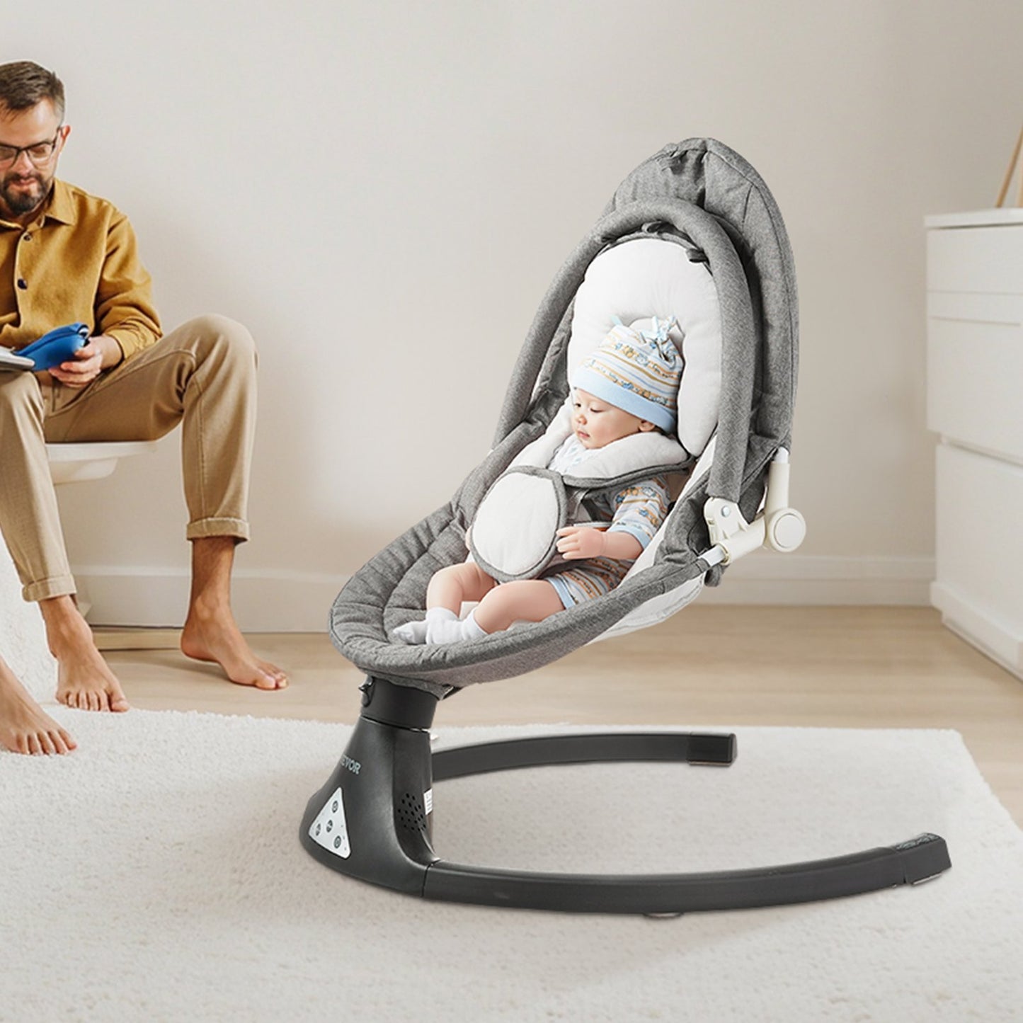 Baby in a gray baby swing with a man sitting nearby in a home setting.