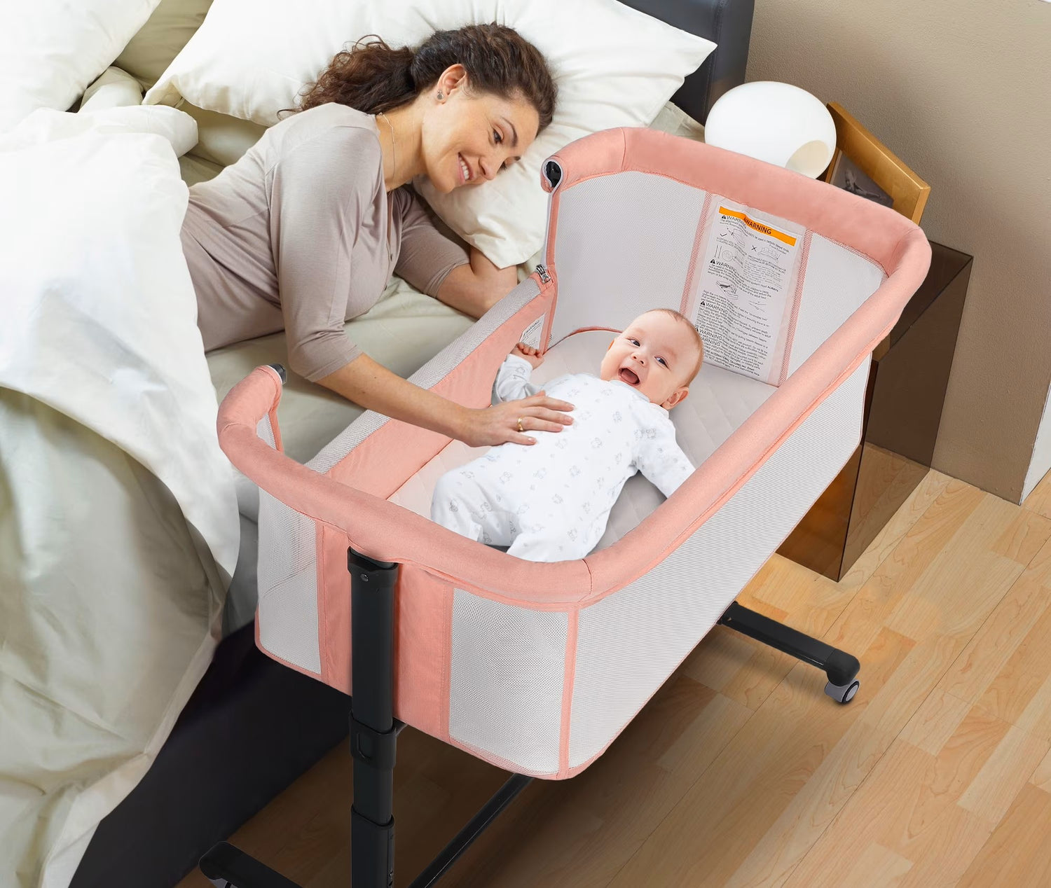 Baby in a portable crib next to a woman lying on a bed