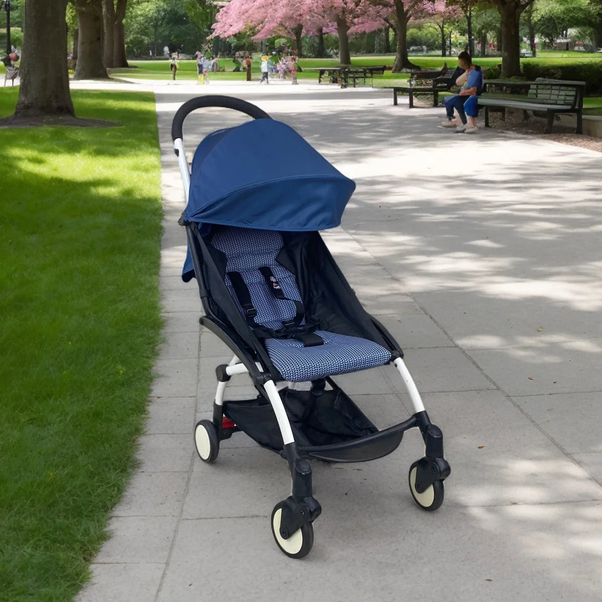 Blue stroller on a sidewalk in a park with green grass and trees.