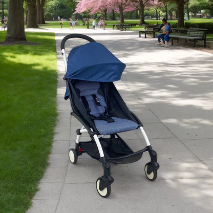 Blue stroller on a sidewalk in a park with green grass and trees.