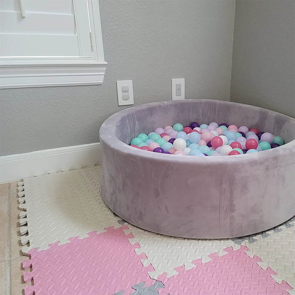 Purple ball pit filled with colorful balls in a room with gray walls and pink floor mats.
